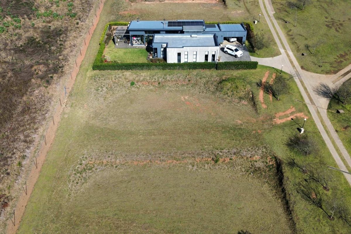 Aerial view of a residential vacant land plot adjacent to an existing modern home with established landscaping and driveway access.