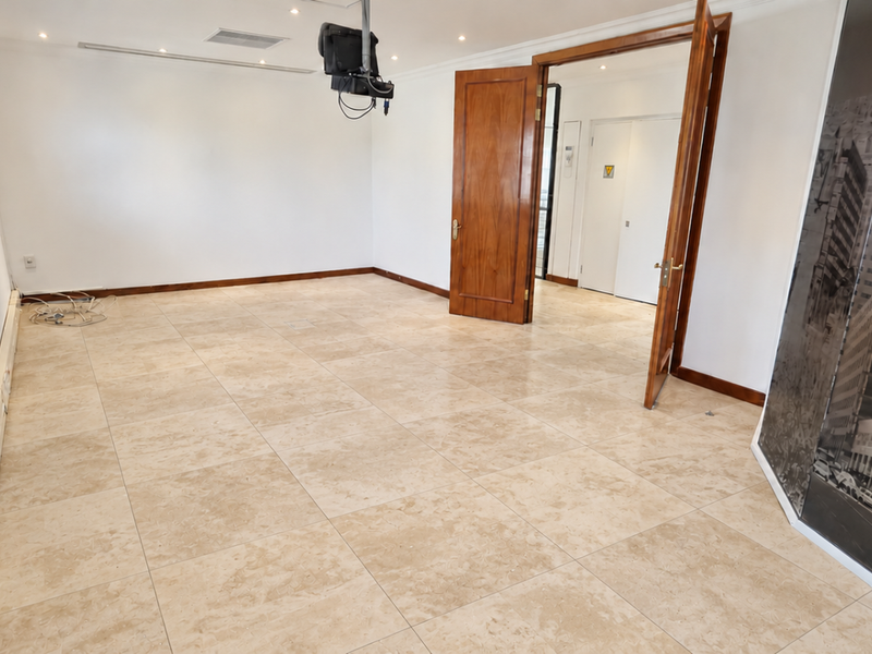 A spacious, empty office suite featuring neutral tiled flooring, recessed lighting, and timber double doors, providing a clean and professional workspace environment.