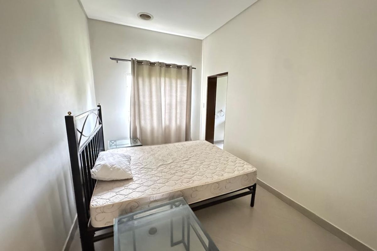 A simple bedroom featuring neutral wall tones, tiled flooring, and a window with curtain fixtures, providing a clean and functional living space.