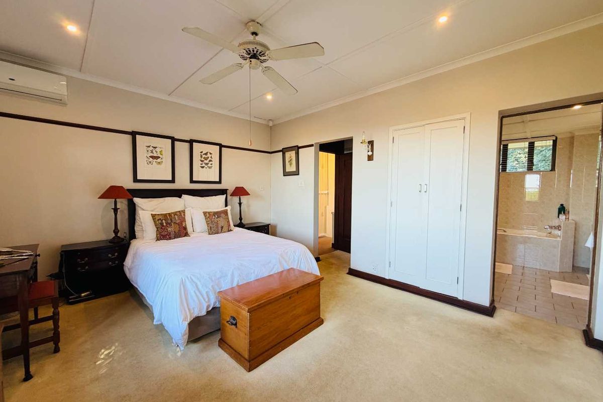 Spacious bedroom featuring a ceiling fan, wall-mounted air conditioning unit, built-in cupboards, and an en-suite bathroom with tiled flooring.