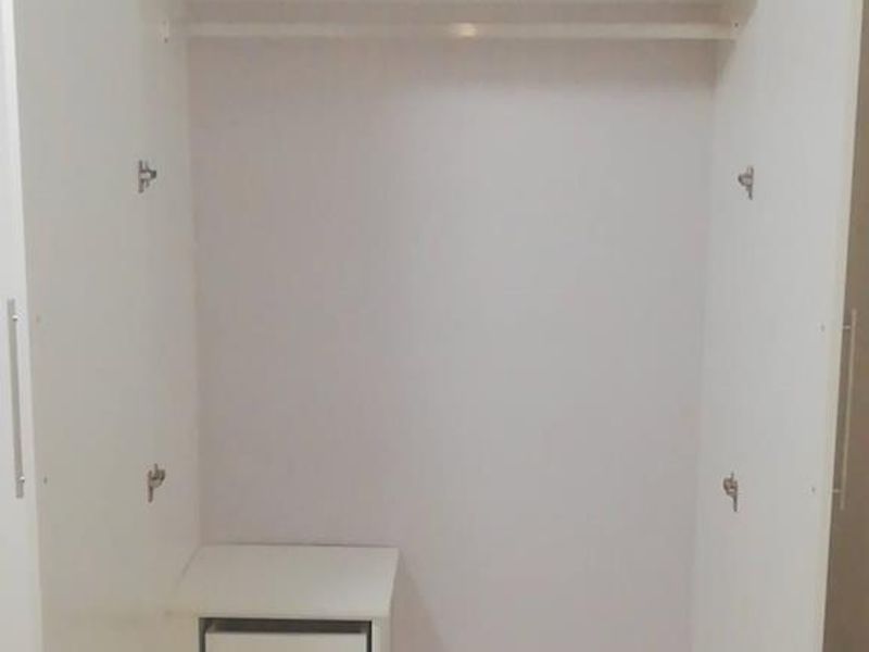 A clean, white built-in wardrobe featuring an internal hanging rail and integrated drawer storage.