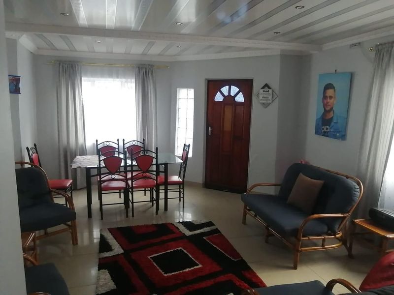 A combined living and dining area featuring tiled flooring, a panelled ceiling with recessed lighting, and a solid timber entrance door.
