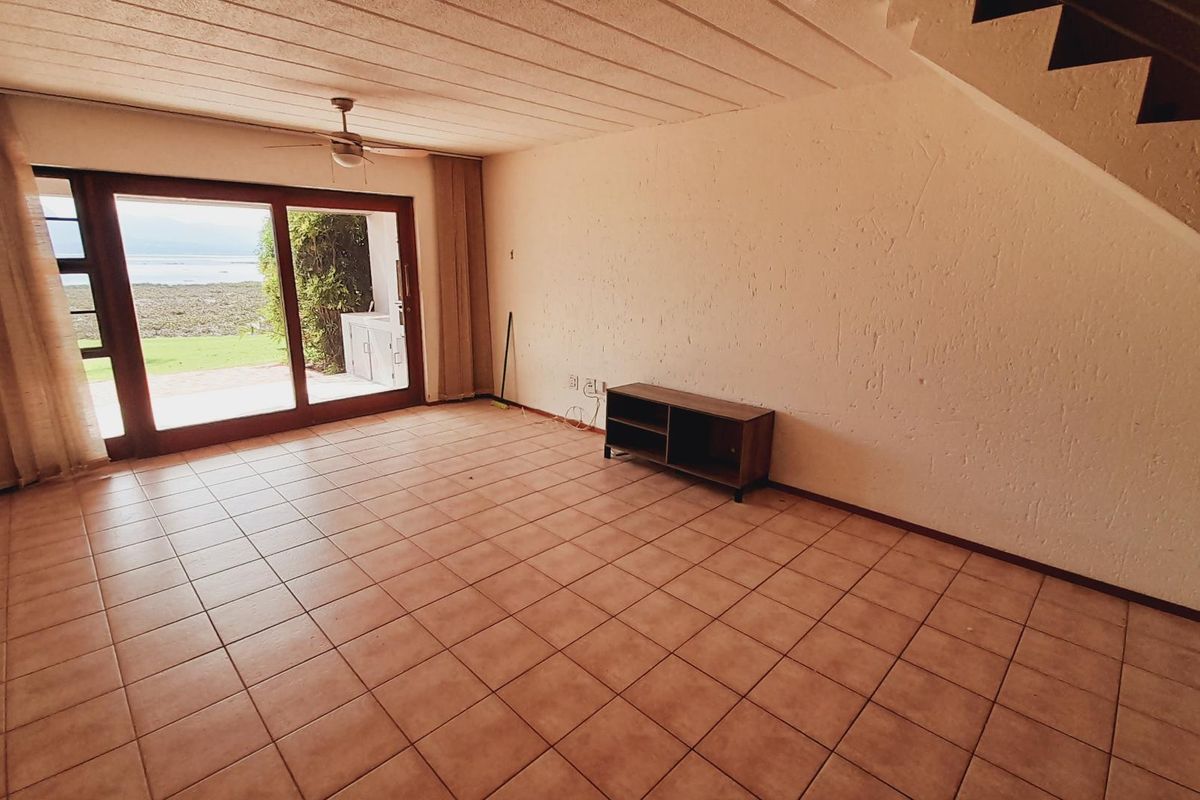 Spacious living area featuring tiled flooring, a ceiling fan, and large sliding glass doors providing access to the outdoor patio and garden views.