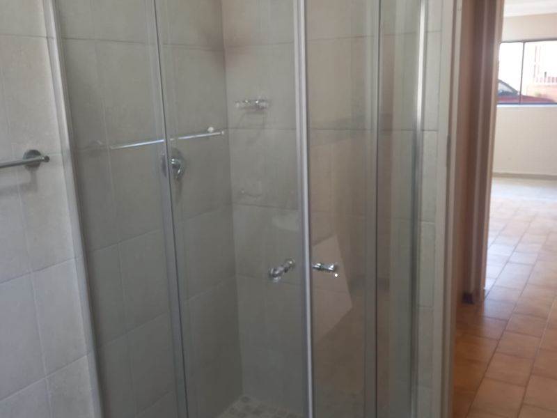 A clean bathroom featuring a modern glass shower enclosure with tiled walls and flooring, providing a functional and well-maintained space.
