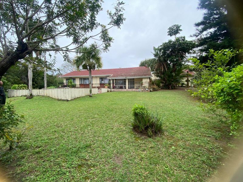 Rear view of a single-story house featuring a tiled roof, a paved patio area with metal balustrades, and a spacious lawn with established trees.