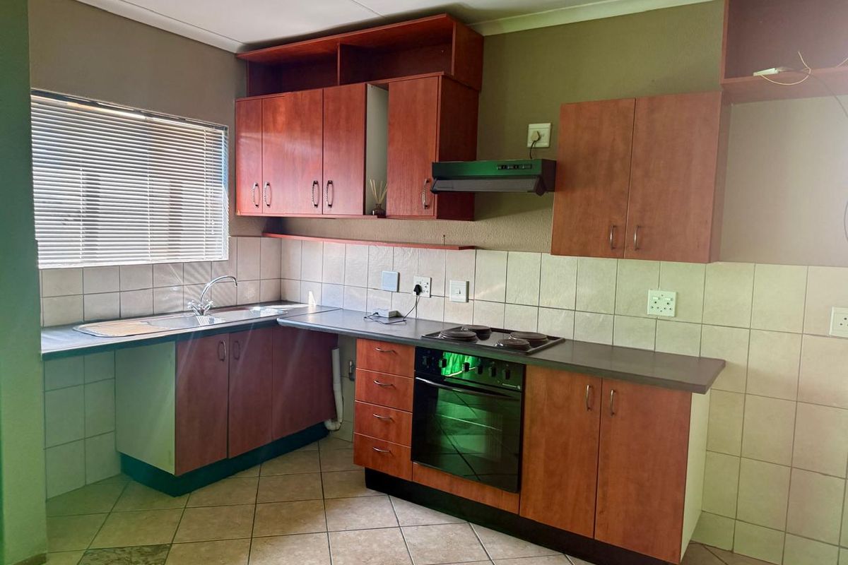 A functional kitchen featuring wooden cabinetry, a built-in oven and hob, extractor fan, and tiled splashbacks with a stainless steel sink.