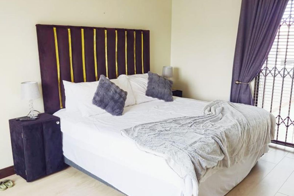 A well-maintained bedroom featuring light-toned laminate flooring, a ceiling fan, and a security gate leading to the exterior.