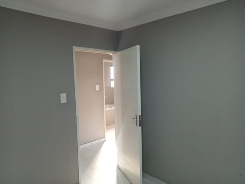 A clean, empty bedroom featuring neutral grey walls, coving, and a modern internal door leading to an adjacent bathroom area.