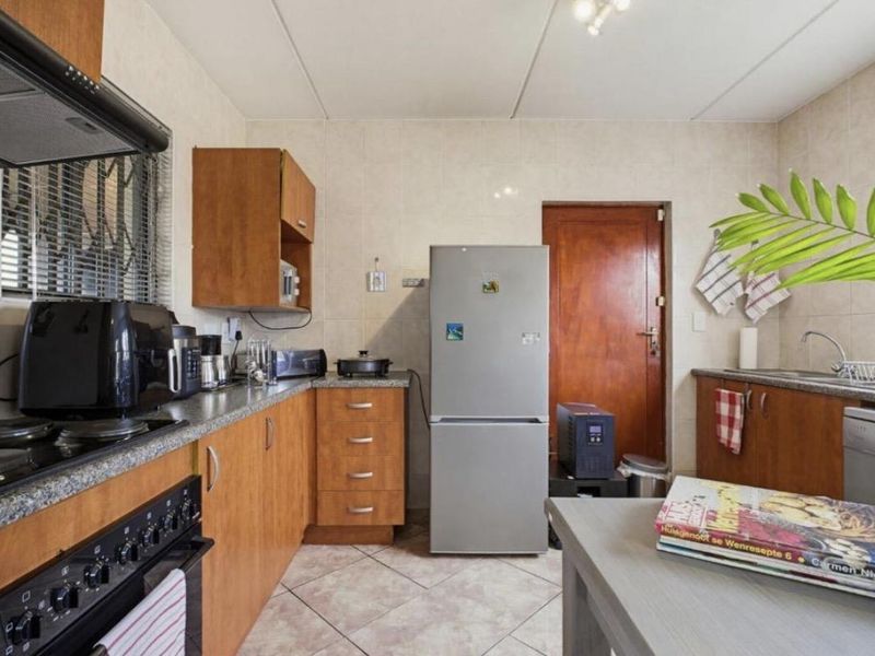 A functional kitchen featuring wooden cabinetry, laminate countertops, a built-in oven with extractor fan, and tiled finishes throughout.
