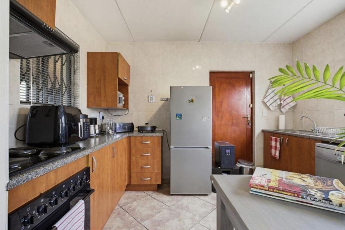 A functional kitchen featuring wooden cabinetry, laminate countertops, a built-in oven with extractor fan, and tiled finishes throughout.