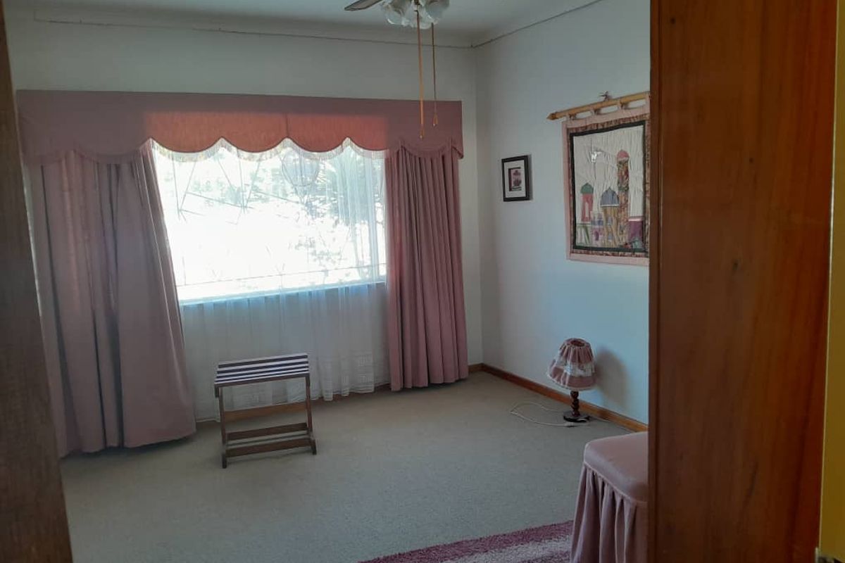 A bedroom featuring neutral carpeting, a ceiling fan, and large windows with traditional drapery.