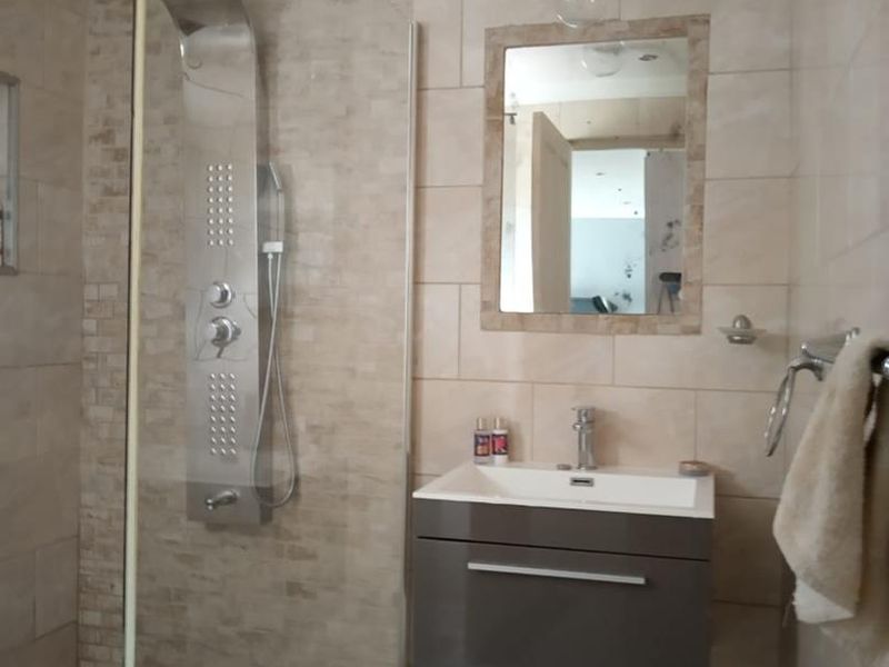 Modern bathroom featuring a walk-in shower with a stainless steel shower panel, wall-mounted vanity unit, and neutral tiled finishes.