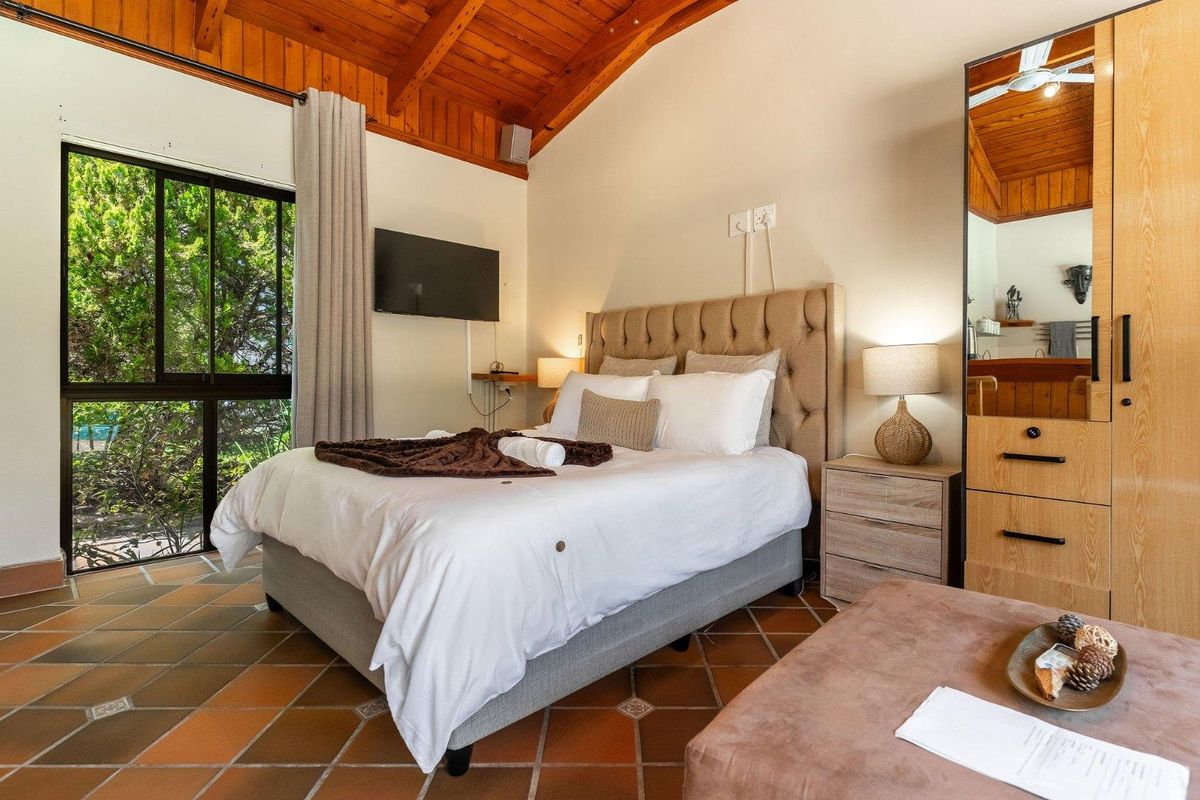 A cozy bedroom featuring an exposed timber vaulted ceiling, terracotta tiled flooring, and a sliding glass door providing natural light and garden views.