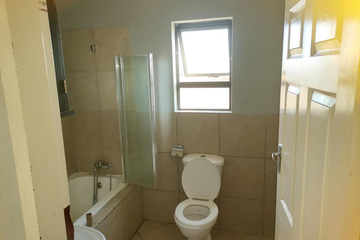 A functional bathroom featuring a bathtub with a glass shower screen, a toilet, and tiled flooring and wall accents.