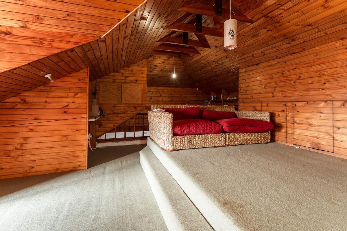 Attic-style bedroom featuring extensive timber-clad walls and ceilings, exposed rafters, and a raised carpeted platform with built-in storage.