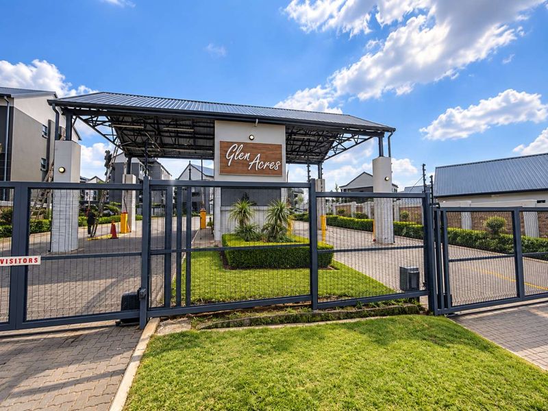 The secure entrance to Glen Acres apartment complex, featuring a gated access point, paved driveway, and well-maintained landscaped garden.