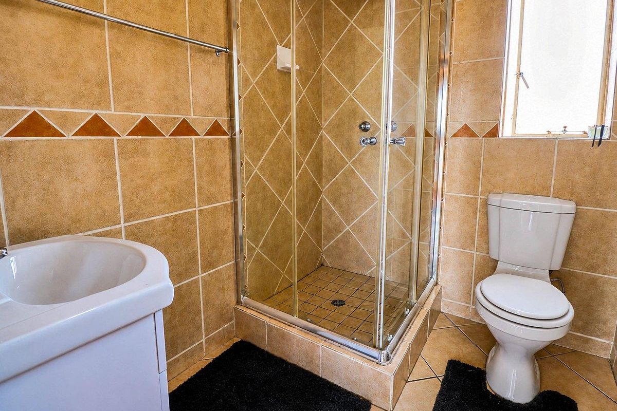 A functional bathroom featuring a glass-enclosed shower, a standard toilet, and a vanity basin with neutral-toned wall and floor tiling.
