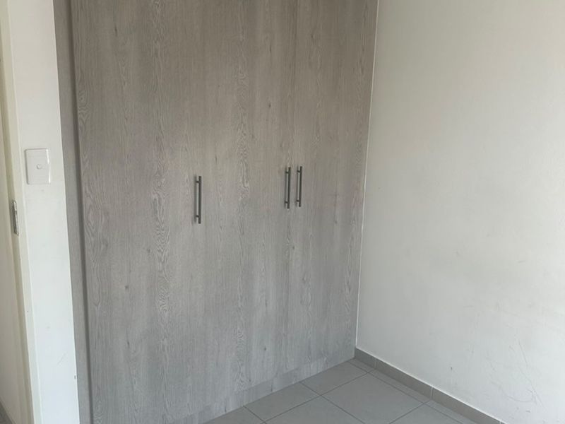 A clean, empty bedroom featuring modern wood-look built-in wardrobes and neutral tiled flooring, providing a versatile space ready for personalization.