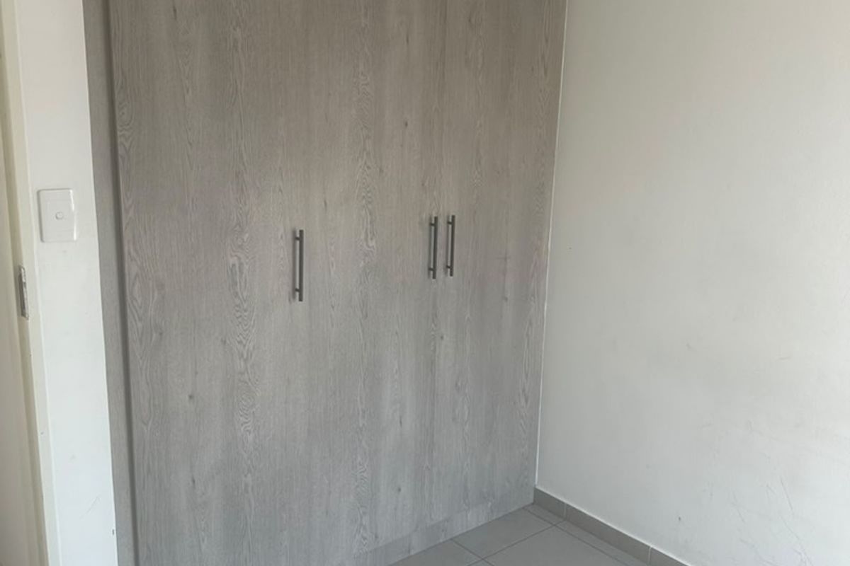 A clean, empty bedroom featuring modern wood-look built-in wardrobes and neutral tiled flooring, providing a versatile space ready for personalization.