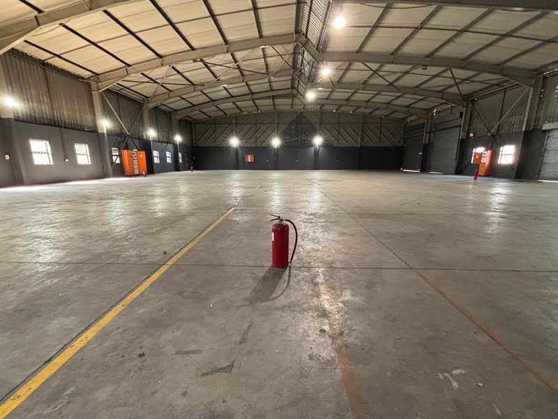 Spacious industrial warehouse featuring high ceilings with exposed steel trusses, polished concrete flooring, and integrated industrial lighting throughout the open floor plan.