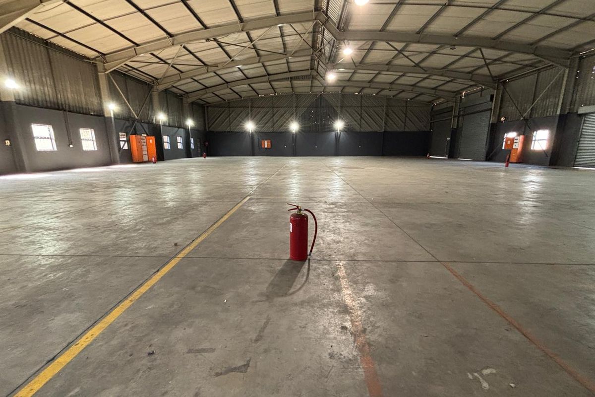 Spacious industrial warehouse featuring high ceilings with exposed steel trusses, polished concrete flooring, and integrated industrial lighting throughout the open floor plan.