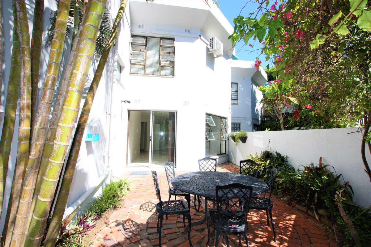 A private rear courtyard featuring brick paving, established garden beds, and direct access to the townhouse interior via a sliding glass door.