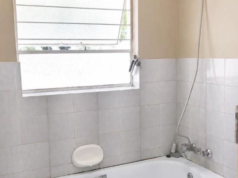A functional bathroom featuring a built-in bathtub with a handheld shower attachment, tiled splashback, and a louver window for natural ventilation.