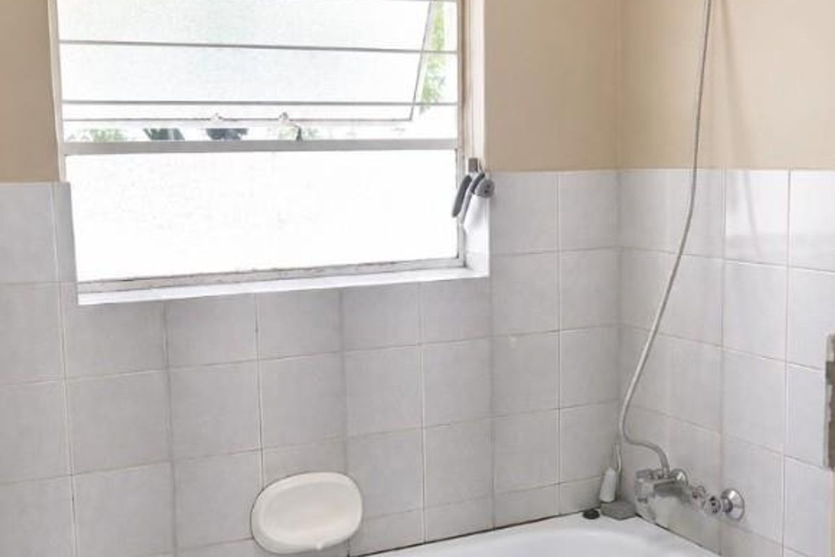 A functional bathroom featuring a built-in bathtub with a handheld shower attachment, tiled splashback, and a louver window for natural ventilation.