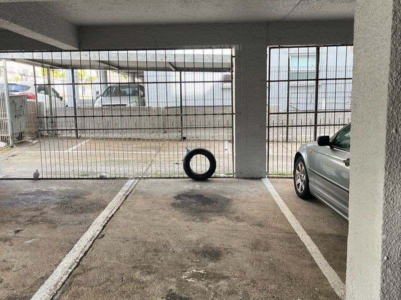 A covered parking bay featuring concrete flooring, support pillars, and a secure metal gate enclosure.