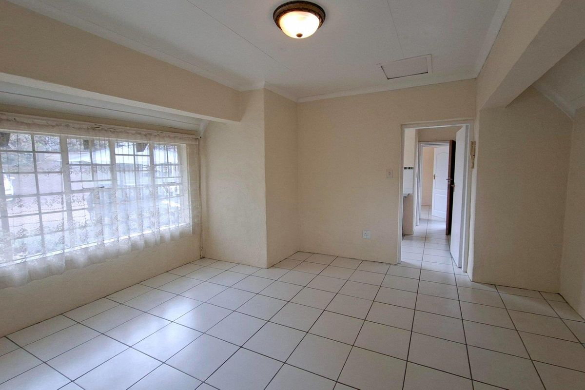 A bright, empty living room featuring neutral tiled flooring, coved ceilings, and a large window, providing a clean canvas for interior design.