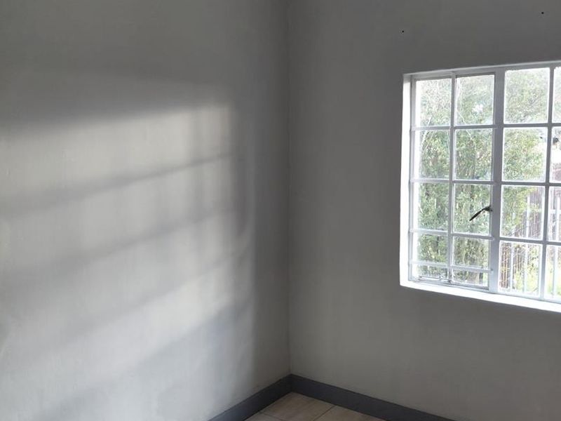 A clean, empty bedroom featuring neutral grey walls, tiled flooring, and a window with security bars, providing a blank canvas for personalization.