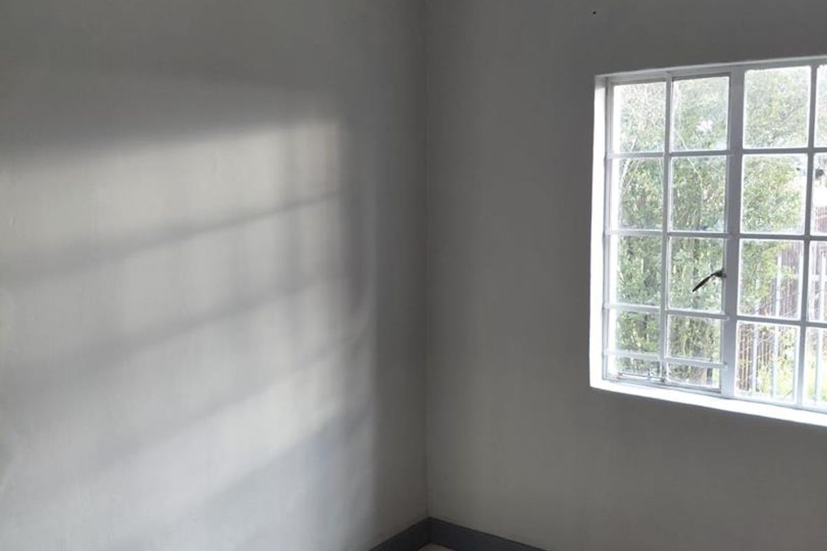 A clean, empty bedroom featuring neutral grey walls, tiled flooring, and a window with security bars, providing a blank canvas for personalization.