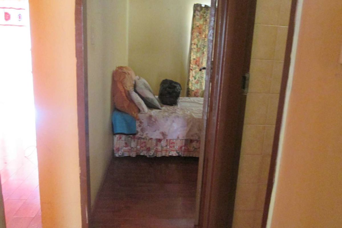 A view through a doorway into a bedroom featuring laminate flooring and dated wall finishes, requiring cosmetic updates.