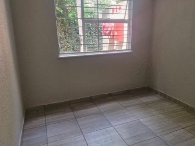 A vacant bedroom featuring neutral tiled flooring and a window fitted with security bars, offering a clean and simple space.