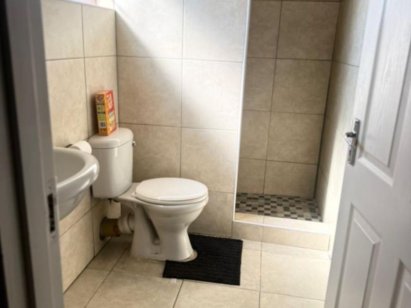 A functional bathroom featuring a walk-in shower, pedestal basin, and neutral ceramic tiling throughout.