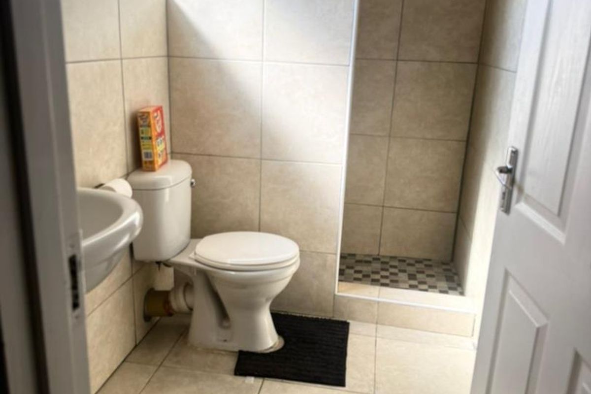 A functional bathroom featuring a walk-in shower, pedestal basin, and neutral ceramic tiling throughout.