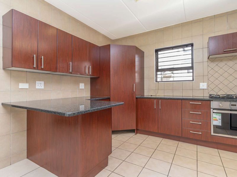 A functional kitchen featuring dark wood cabinetry, granite countertops, built-in oven, gas hob, and tiled finishes throughout.