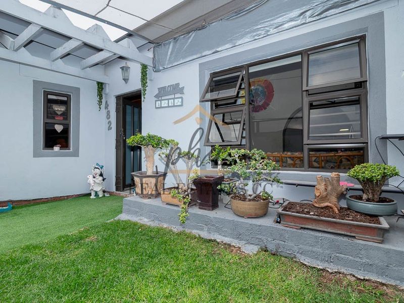 Front entrance area featuring a concrete porch, pergola structure, and aluminium window frames, with a small lawn and garden space.
