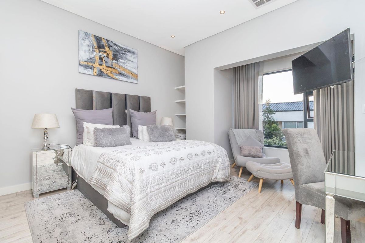 A well-maintained bedroom featuring light laminate flooring, recessed downlighting, and a built-in shelving unit, with a large window providing natural light.