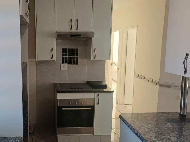 Compact kitchen featuring white cabinetry, built-in oven and hob, extractor fan, and durable tiled flooring with granite-look countertops.