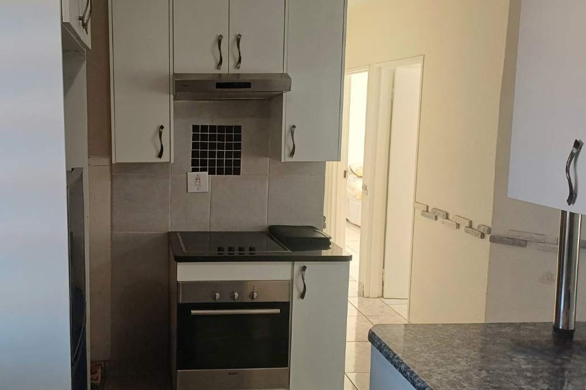 Compact kitchen featuring white cabinetry, built-in oven and hob, extractor fan, and durable tiled flooring with granite-look countertops.