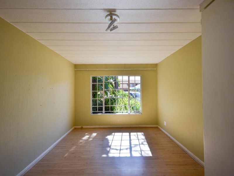 An empty bedroom featuring laminate flooring, ceiling tiles, and a window with security burglar bars.