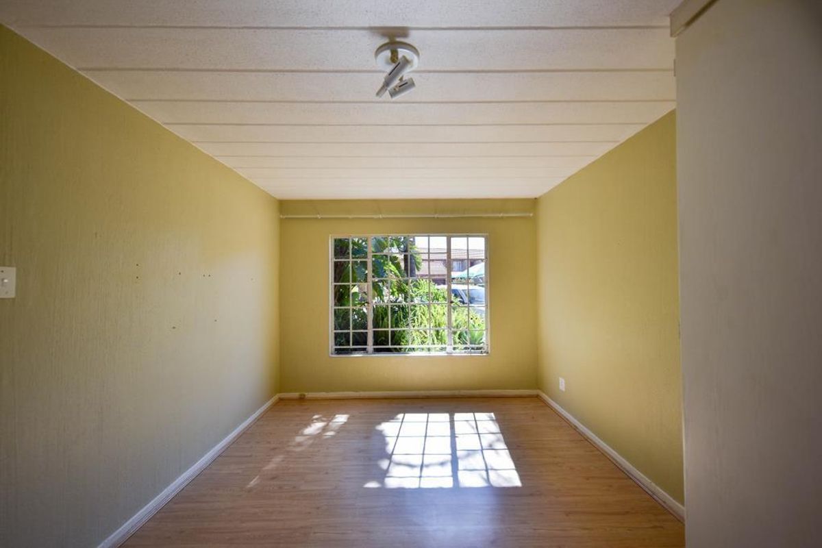 An empty bedroom featuring laminate flooring, ceiling tiles, and a window with security burglar bars.