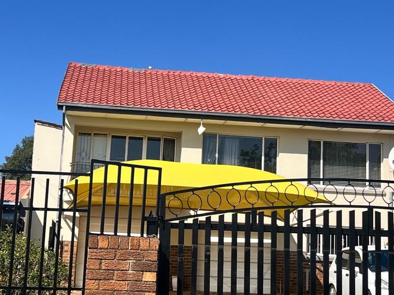 Front elevation of a cottage featuring a tiled roof, metal security gate, and a prominent yellow shade sail over the driveway area.