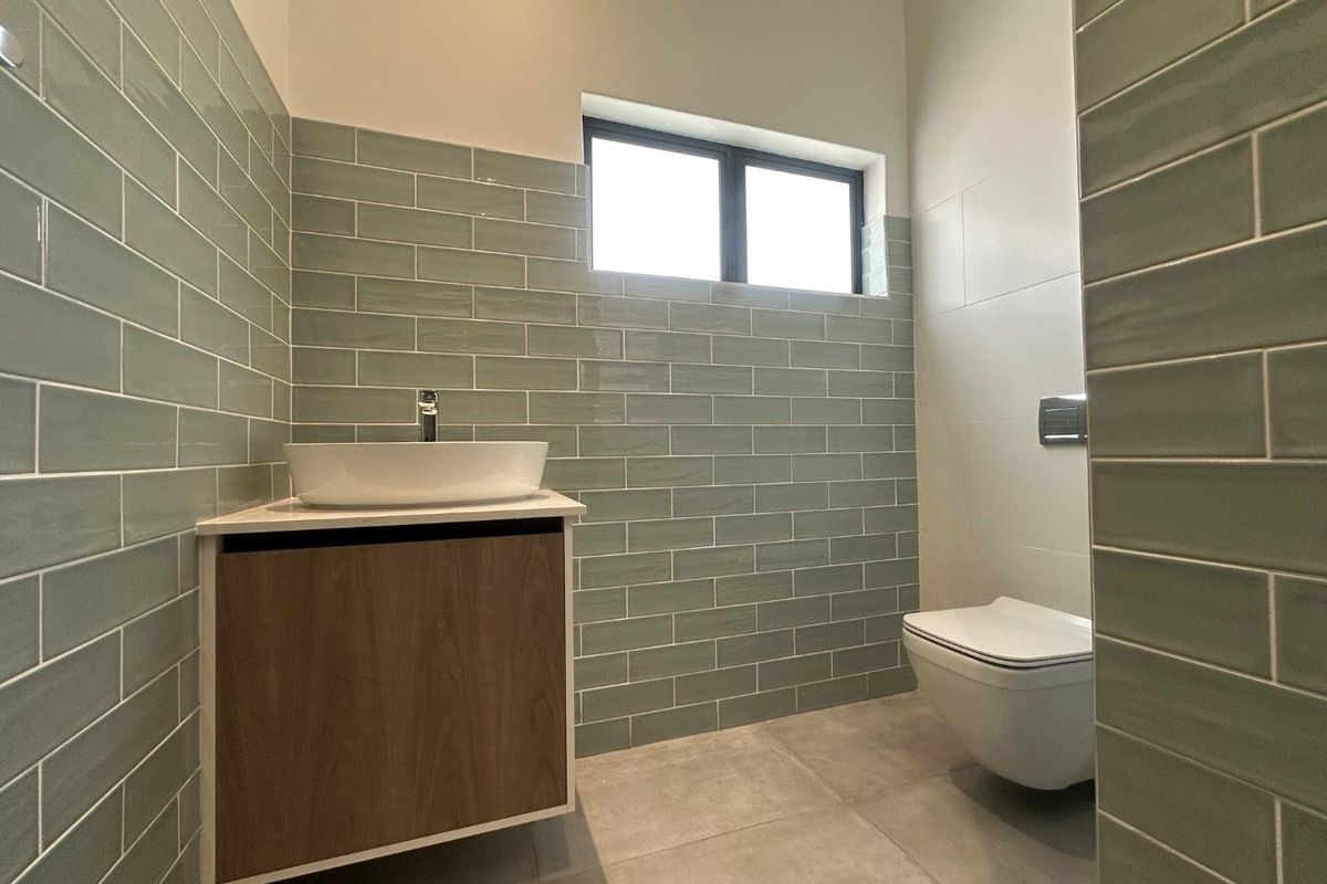 Modern bathroom featuring sage green subway wall tiles, a floating wood-finish vanity with a vessel sink, and a wall-hung toilet.