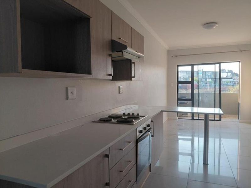 Modern kitchen featuring light wood cabinetry, built-in oven and hob, breakfast bar, and tiled flooring, leading to an outdoor balcony area.
