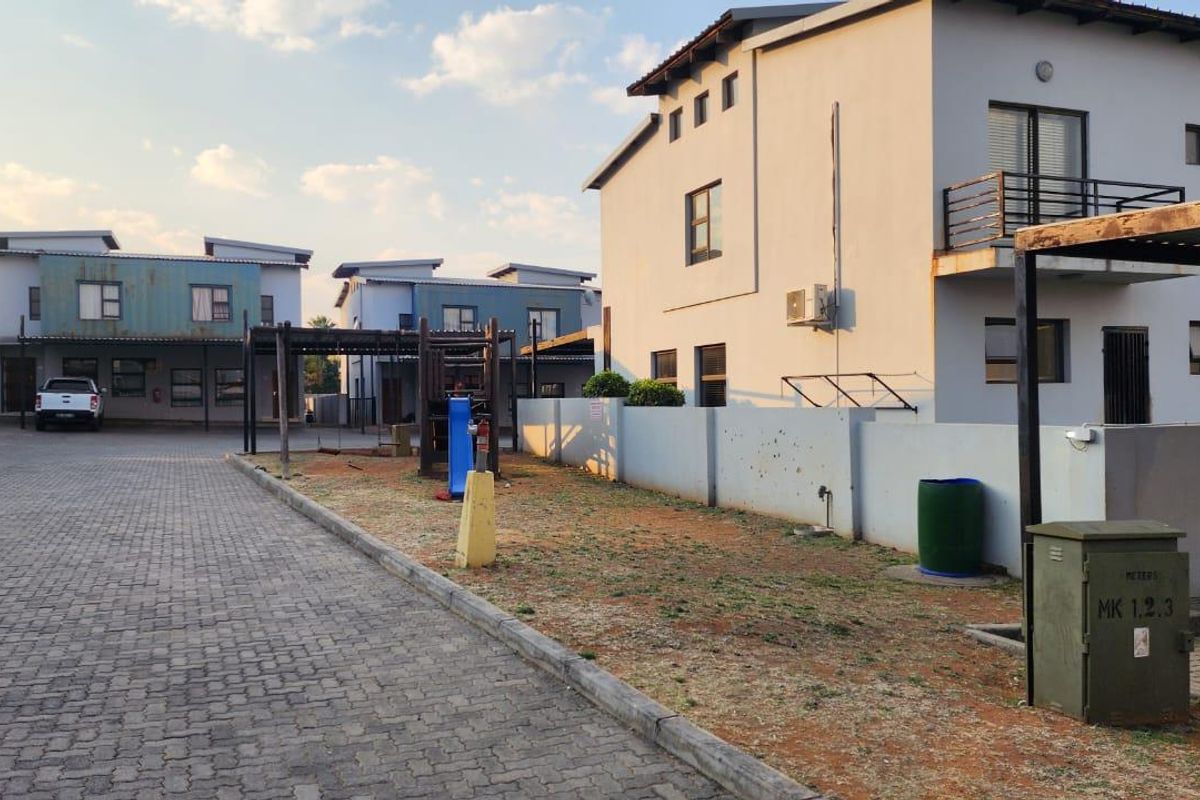 Exterior view of an apartment complex featuring a paved driveway, communal lawn area, and multi-story residential buildings with balconies.