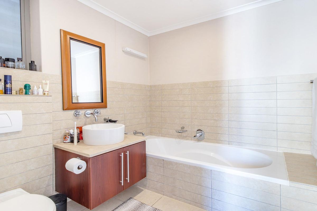 A well-maintained bathroom featuring a built-in bathtub, a modern vessel sink on a wooden vanity, and neutral wall tiling.
