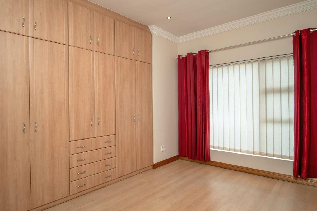 A bright, empty bedroom featuring extensive built-in wooden cupboards, laminate flooring, and coved ceilings, offering a clean and versatile space.