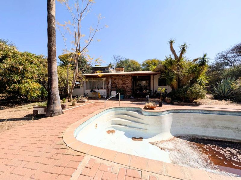 Rear exterior view featuring a swimming pool with brick paving and a covered patio area attached to the main house structure.